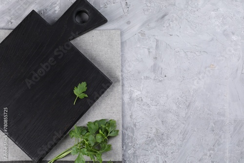 Wooden cutting board, fresh parsley and napkin on grey table, top view. Space for text