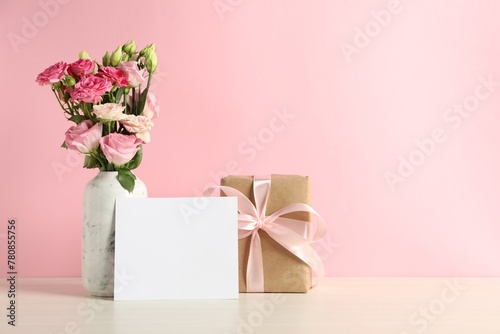 Happy Mother's Day. Gift box, blank card and bouquet of beautiful flowers in vase on white table against pink background. Space for text