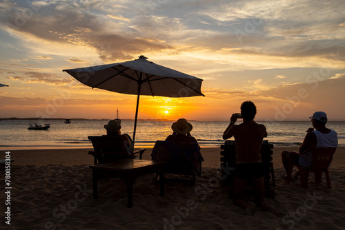 Silhueta de pessoas na praia olhando e fotografando o pôr-do-sol durante o entardecer em uma praia do nordeste brasileiro