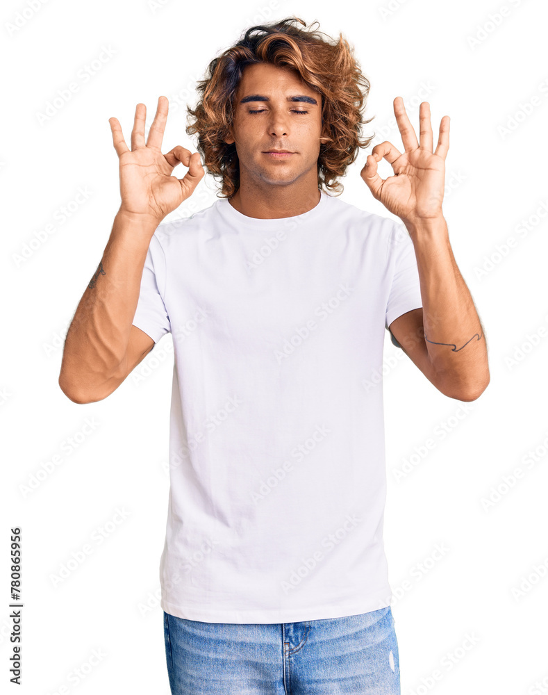 Young hispanic man wearing casual white tshirt relaxed and smiling with eyes closed doing meditation gesture with fingers. yoga concept. Young hispanic man wearing casual white tshirt relaxed and smiling with eyes closed doing meditation gesture with fingers. yoga concept.
