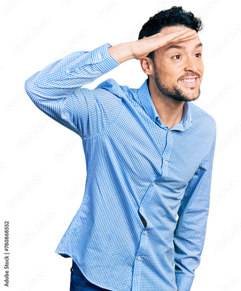 Hispanic man with beard wearing casual business shirt very happy and smiling looking far away with hand over head. searching concept. Hispanic man with beard wearing casual business shirt very happy and smiling looking far away with hand over head. searching concept.