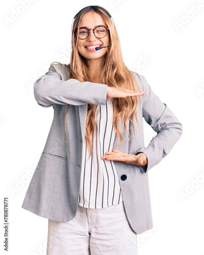 Young beautiful blonde woman wearing call center agent headset gesturing with hands showing big and large size sign, measure symbol. smiling looking at the camera. measuring concept. photo