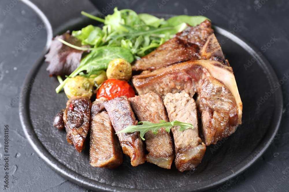 Delicious grilled beef meat, vegetables and greens on black table, closeup
