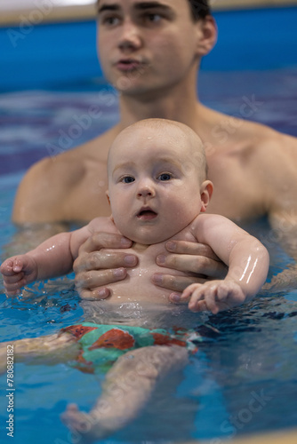 Portrait of the curious baby with a swim coach in a swimming pool. Swimming lessons for newborns. Closeup.