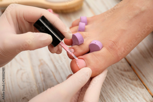 Professional pedicurist painting client s toenails with polish in beauty salon  closeup
