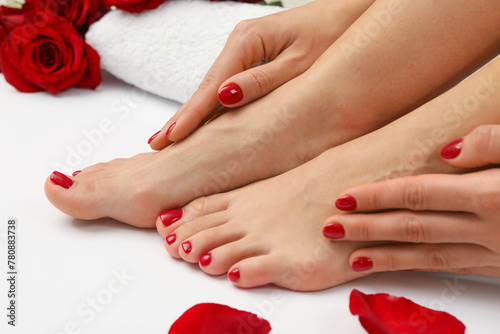 Woman with stylish red toenails after pedicure procedure and rose petals on white background, closeup