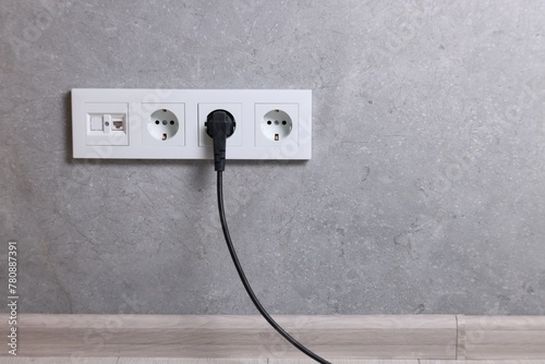 Power sockets and electric plug on grey wall, space for text photo