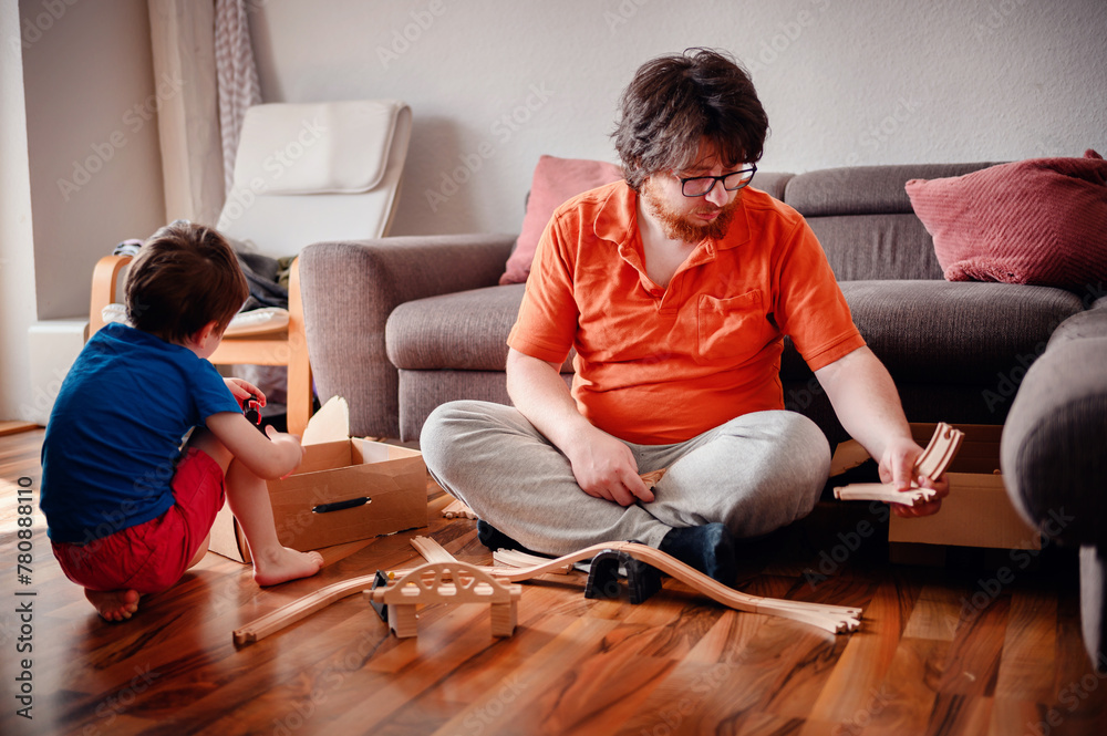 A child and an adult are absorbed in assembling a wooden toy train set on the floor, enjoying a playful and educational moment together