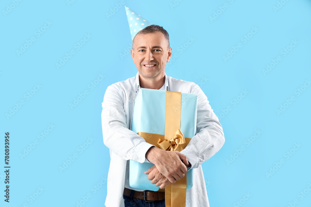 Mature man in party hat with birthday gift on blue background Mature man in party hat with birthday gift on blue background