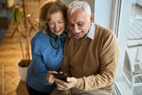 Happy senior couple talking while using mobile phone at home 