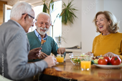 Group of happy mature friends talking while having a meal at dining table. 