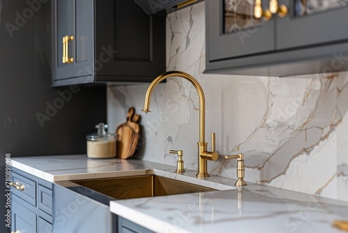 Detailed photo of kitchen sink with gold faucet marble backsplash grey cabinets and gold hardware