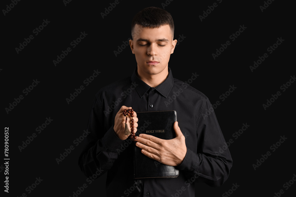 Young man with rosary beads and Bible praying on black background Young man with rosary beads and Bible praying on black background