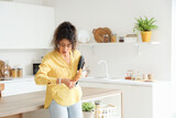 Hurrying young African-American woman with croissant and laptop looking at wristwatch in kitchen