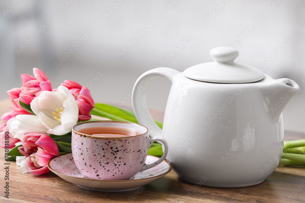 Cup of hot brewed tea, pot and flowers on table against blurred background