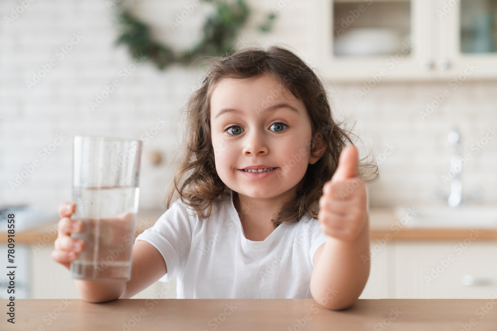 Cute little caucasian girl daughter showing thumb up drinking water, holding a glass of water, hydration, healthy eating habits, daily consumption rate , intake Cute little caucasian girl daughter showing thumb up drinking water, holding a glass of water, hydration, healthy eating habits, daily consumption rate , intake