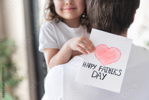 Cropped shot of a cheerful small kid daughter holding greeting card for her father to congratulate him with father`s day, make him surprise and gift. Fatherhood. I love you, dad! photo