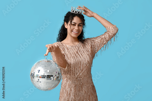 Beautiful young African-American woman in tiara and stylish dress with disco ball on blue background photo