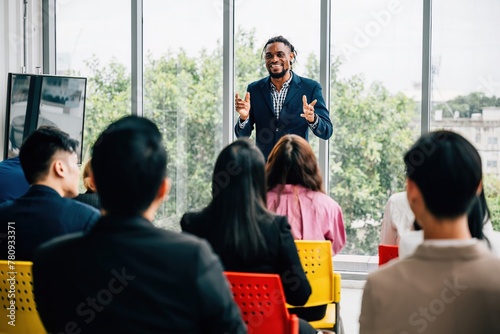 A diverse group of businesspeople convenes in an office meeting. Seated colleagues exchange thoughts, while male and female managers stand, promoting effective teamwork. photo