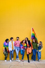 Vertical. Portrait group cheerful young friends standing on wall yellow. LGBT community smiling people on gay pride day enjoying together showing rainbow flags. Gen z and parade party. Copy space