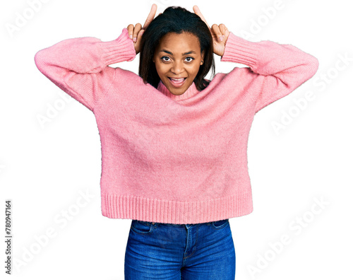 Beautiful hispanic woman wearing casual winter sweater posing funny and crazy with fingers on head as bunny ears, smiling cheerful