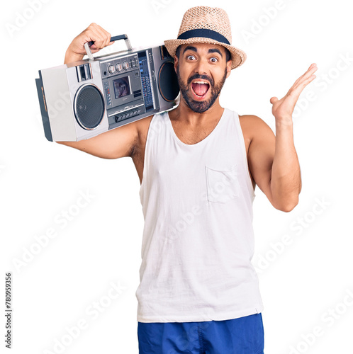 Young hispanic man holding boombox, listening to music celebrating victory with happy smile and winner expression with raised hands