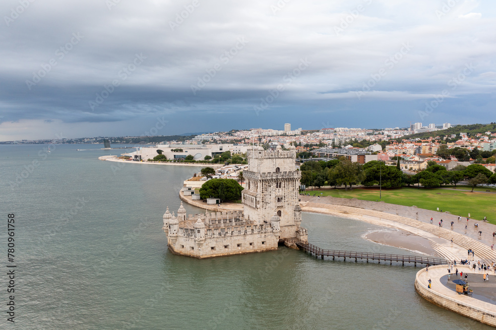 Aerial drone shot of Belem Tower overlooking cityscape. Fortress monument in Lisbon on Tagus River. 16th-century fortification Torre de Belem in city under cloudy sky. Evening time