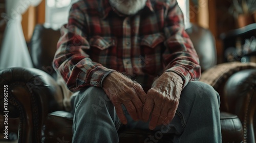 Elderly man grimacing in pain as he sits on the couch, his hand resting on his aching knee, depicts the challenges faced by seniors with health issues.