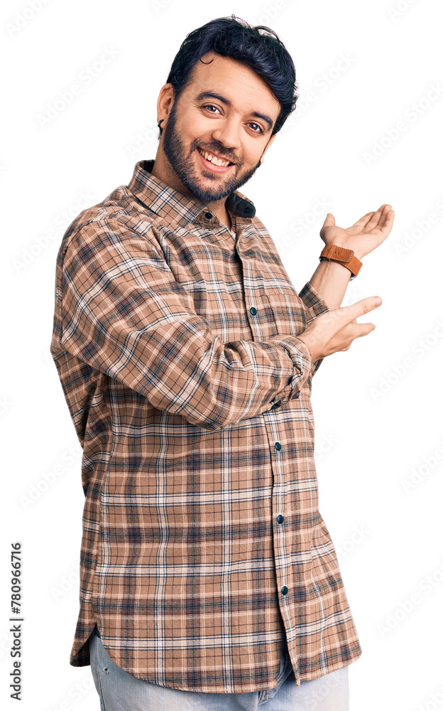 Young hispanic man wearing casual clothes inviting to enter smiling natural with open hand Young hispanic man wearing casual clothes inviting to enter smiling natural with open hand