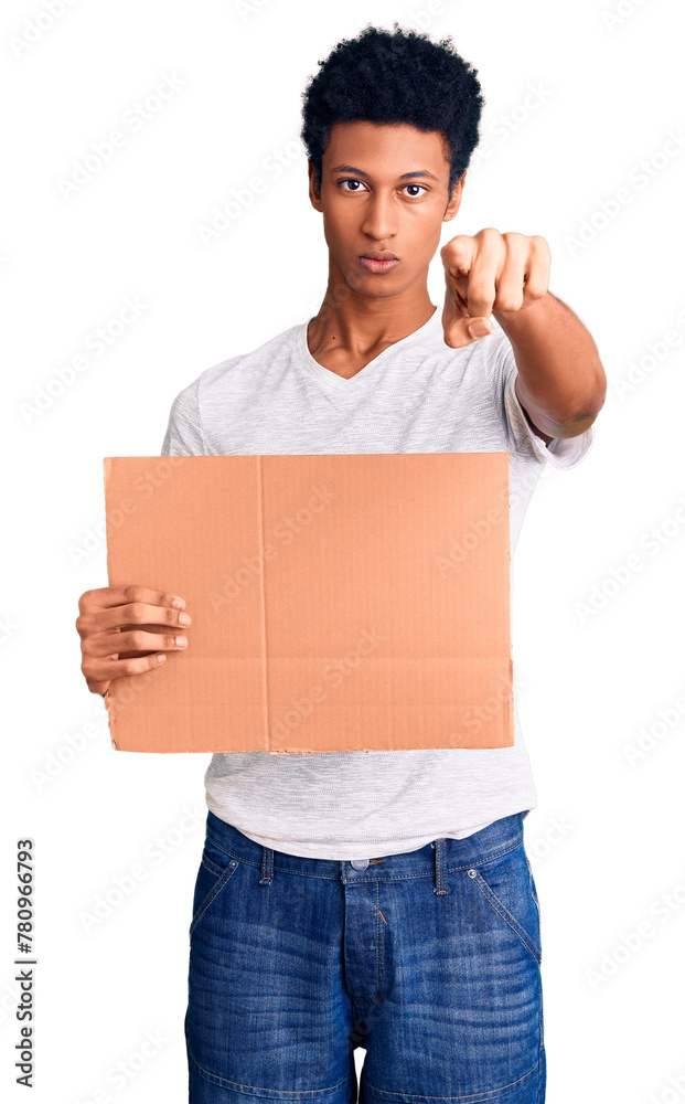 Young african american man holding banner cardboard pointing with finger to the camera and to you, confident gesture looking serious Young african american man holding banner cardboard pointing with finger to the camera and to you, confident gesture looking serious
