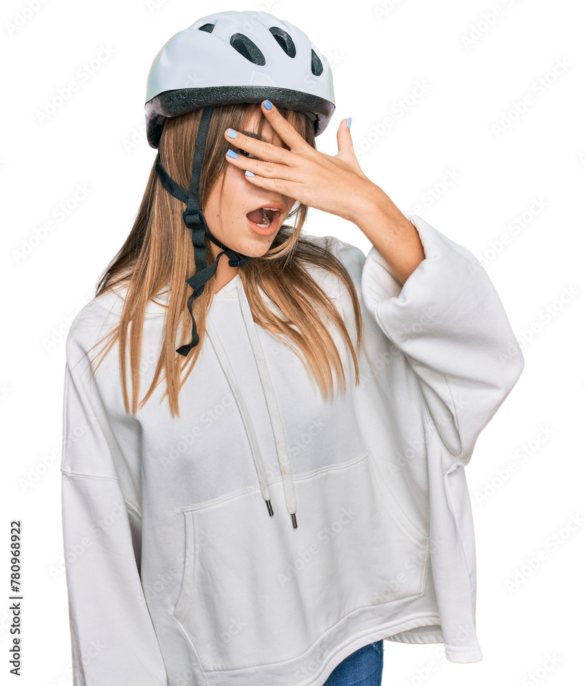 Teenager caucasian girl wearing bike helmet peeking in shock covering face and eyes with hand, looking through fingers with embarrassed expression.
