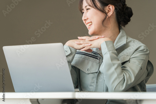 事務所でパソコンの前にいる作業服・作業着姿の若いアジア人ビジネスウーマン（建築士・設計士）
