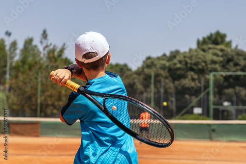 Little boy playing tennis on a dirt court