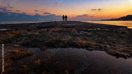 Two people on an old stone pier, sunset on the seashore