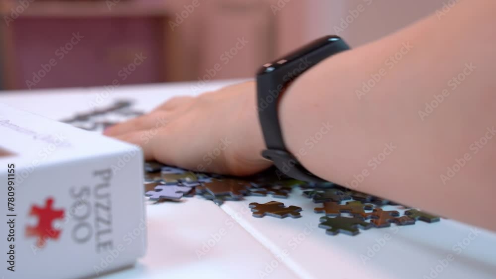 Close-up of hand mixing puzzle pieces on table with white box, fascinating hobby for developing concentration, fine motor skill, memory Exciting relaxing game, development of creative, mental abilitie Close-up of hand mixing puzzle pieces on table with white box, fascinating hobby for developing concentration, fine motor skill, memory Exciting relaxing game, development of creative, mental abilitie