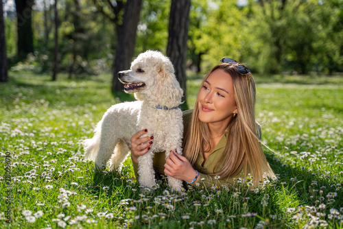 Pretty blonde girl laying on grass in park with her pet poodle 