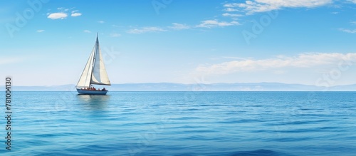 Sailboat peacefully sails on open sea with majestic mountains in the distance