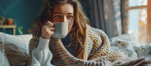 A woman is comfortably wrapped in a cozy blanket while enjoying a warm cup of coffee photo