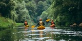 Three people are kayaking down a river. The water is calm and the trees are lush. The kayakers are wearing bright yellow life jackets and helmets