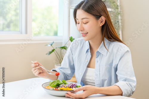 Diet concept, happy asian young woman hand use a fork to prick tomato, fresh vegetable or green salad, eat nutrition food  on table at home, low fat to good body. Girl getting weight loss for healthy. photo