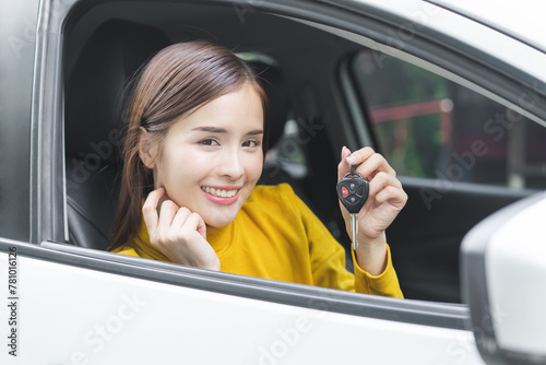 Dealership automobile, happy smile asian young woman sitting in new a car after purchase, rent success, showing, holding auto remote key of vehicle, owner driver guy buy gift for yourself at showroom.