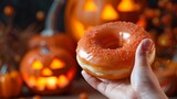 Person holding a glaze doughnut in front of a pumpkin