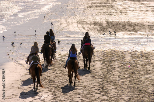 group of people horseback riding on the beach along the ocean © Bill Keefrey