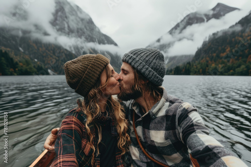 A young couple taking a selfie photo on Lake Braies in Dolomites. The man is wearing a red flannel shirt and grey beanie, the woman wears a white sweater with gray fur hat smiling at the camera © Kien