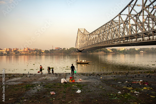 Canvastavla 9th February, 2024, Kolkata, West Bengal, India: Beautiful landscape of a fishing boat on River Ganges crossing Howrah Bridge at the time of sunrise