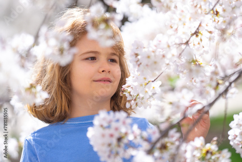 Kids face with flower on the Spring. Child in blooming cherry garden on beautiful spring day. Happy child during spring blossom. Kid in flowered garden. Outdoor Portrait of child near blossoming tree.