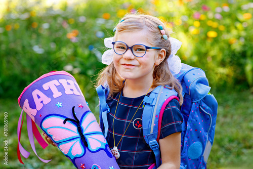 Happy little kid girl with eye glasses with backpack or satchel and big school bag or gift cone traditional in Germany for the first day of school. Healthy adorable child outdoors. Back to school