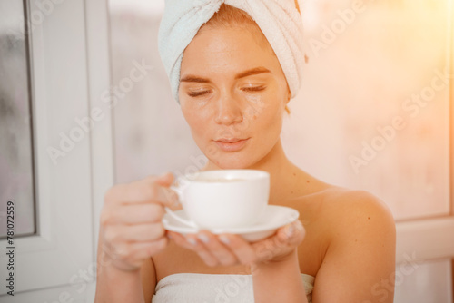 Young serene relaxed woman in spa bath towel drinking hot beverage tea coffee after taking shower bath at home. Beauty treatment, hydration concept.