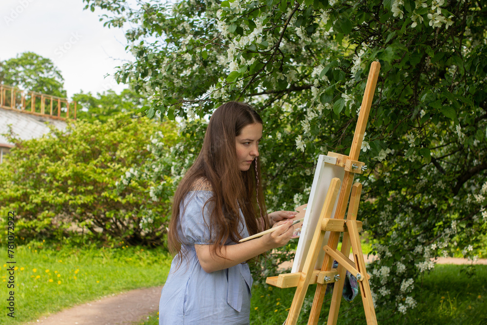 Woman holding palette and brush, female artist painting on canvas on wooden easel. Botanical garden with floral tree Woman holding palette and brush, female artist painting on canvas on wooden easel. Botanical garden with floral tree