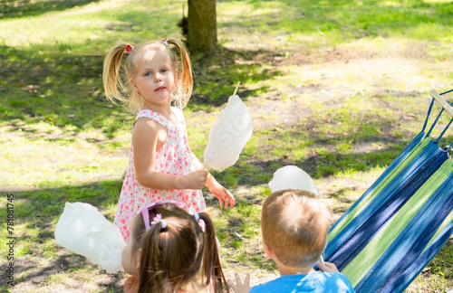 Carefree five-year-old children happily savoring large, fluffy white cotton candy at summer park on a sunny day